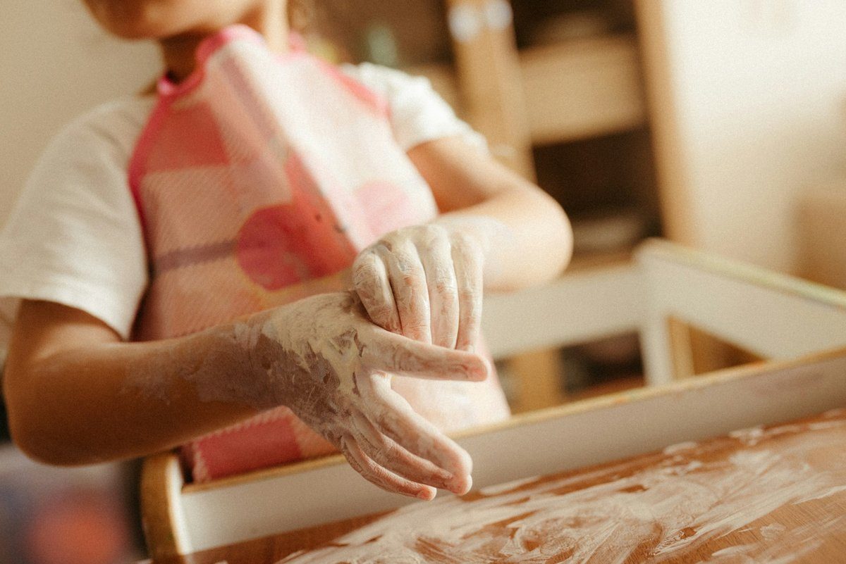 Mains d'enfant couvertes de farine au-dessus d'une planche à pâtisserie