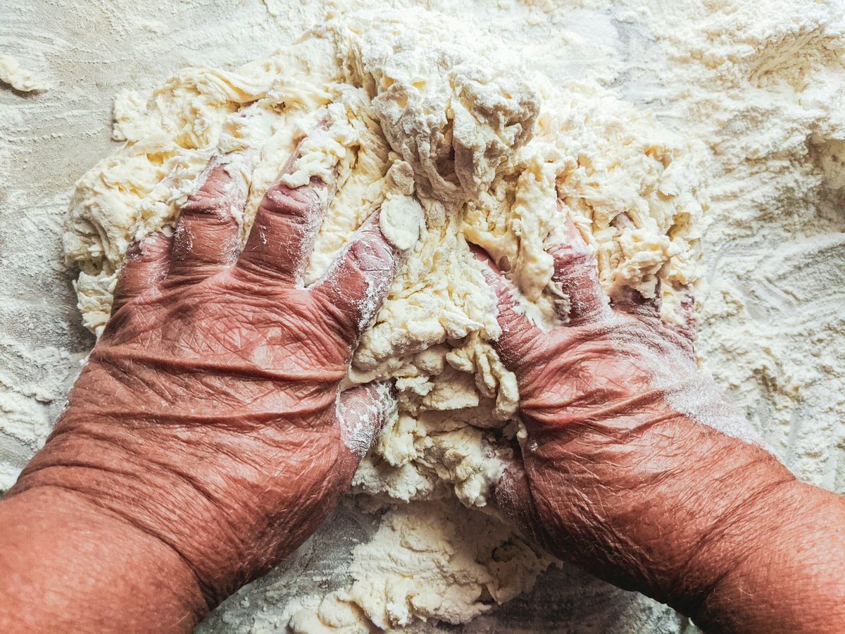 Mains ridées pétrissant une pâte farinée sur une table