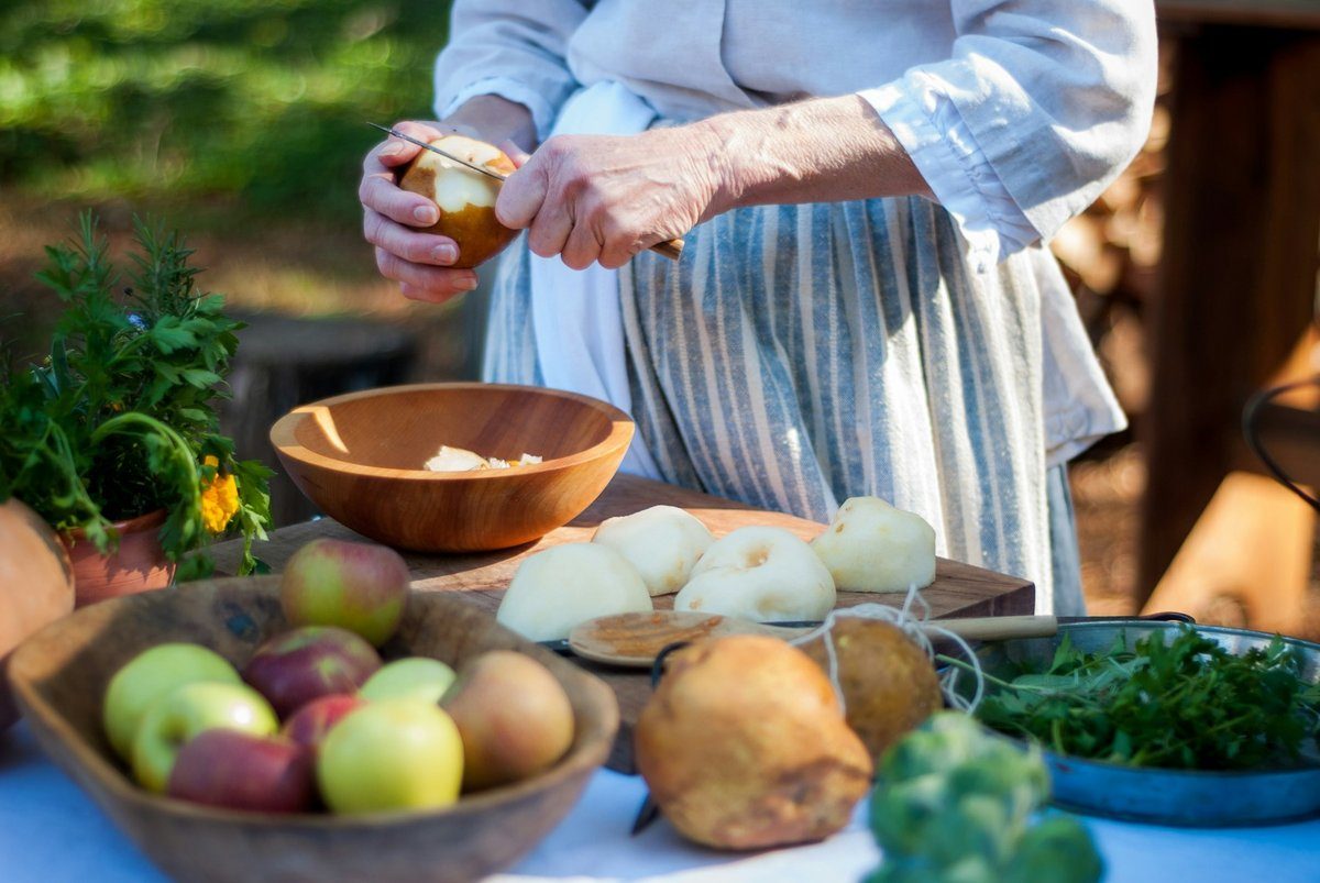 Mains épluchant un fruit au-dessus d'une table garnie de pommes et de légumes